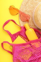 String bag with beach accessories on yellow background, flat lay