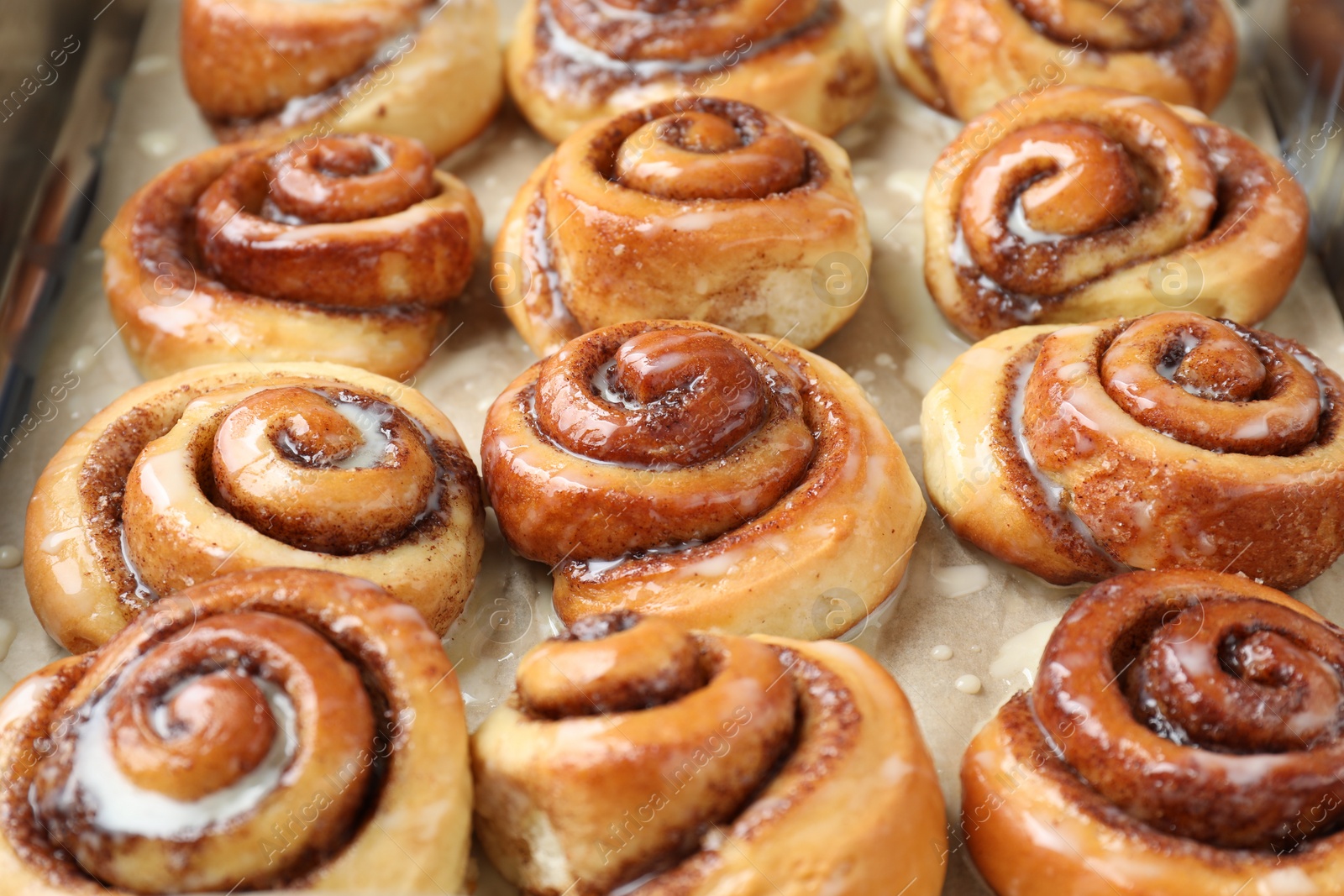 Photo of Tasty cinnamon rolls with cream on parchment paper, closeup