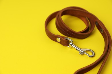 Brown leather dog leash on yellow background, closeup. Space for text