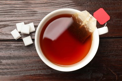Photo of Tea bag in cup and sugar cubes on wooden table, flat lay