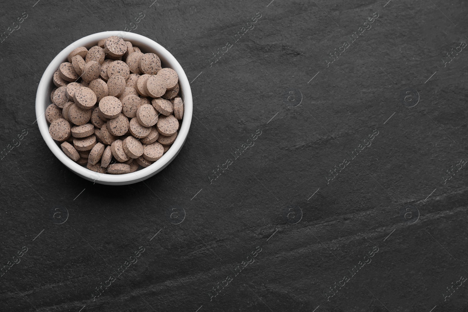 Photo of Brewer's yeast tablets in bowl on black table, top view. Space for text