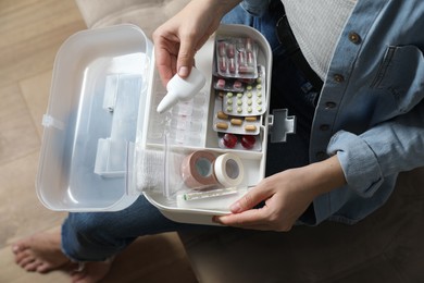 Woman putting medicament into first aid kit indoors, top view