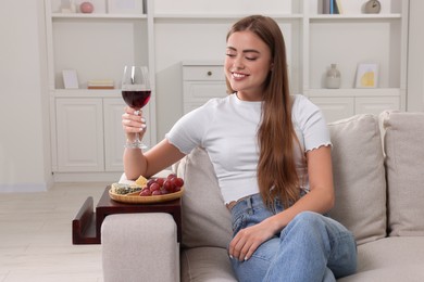 Photo of Happy woman holding glass of wine at home. Snacks on sofa armrest wooden table