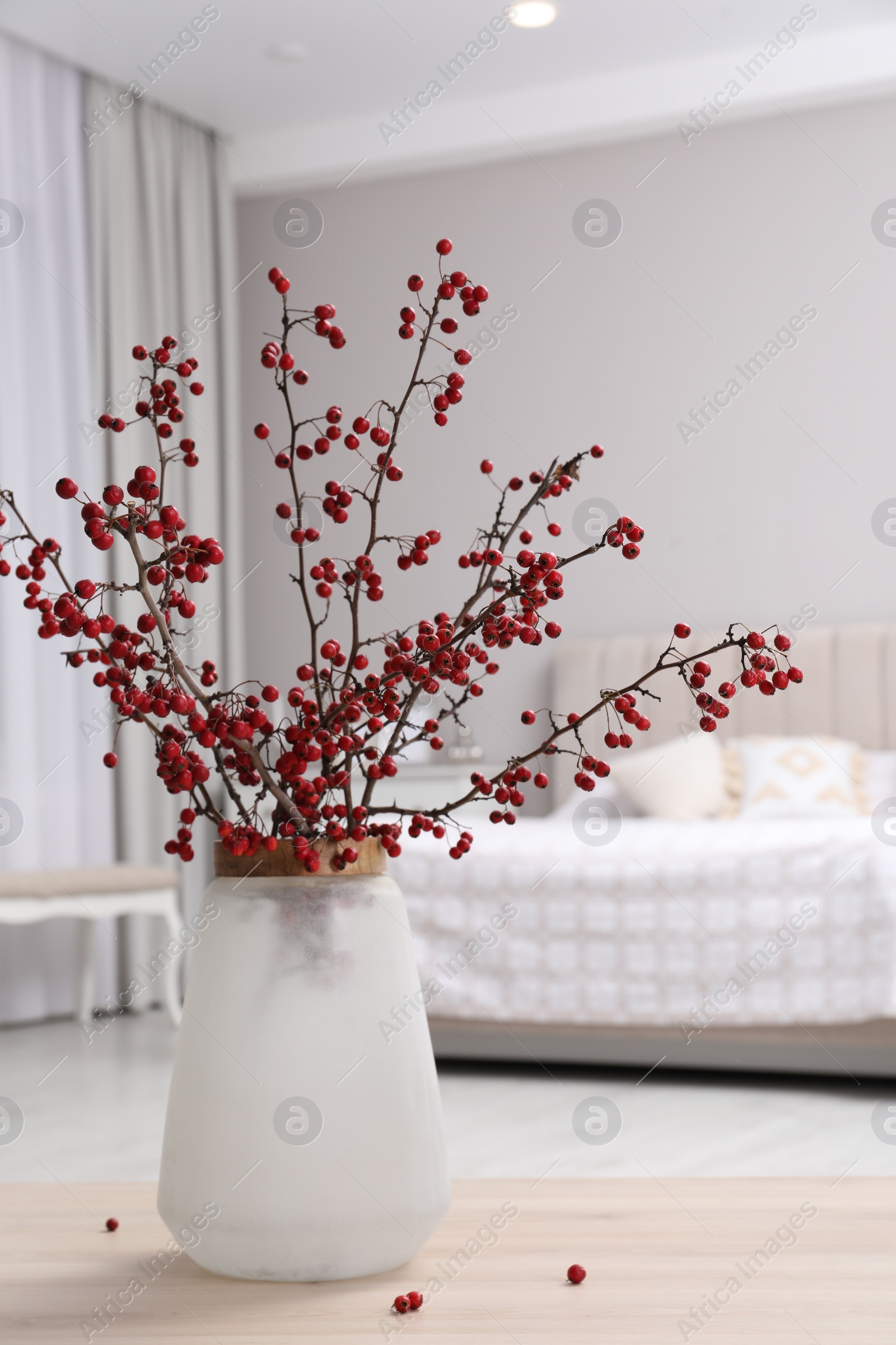 Photo of Hawthorn branches with red berries on wooden table in bedroom