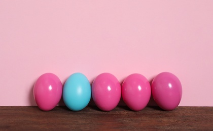 Easter eggs on wooden table against pink background, space for text