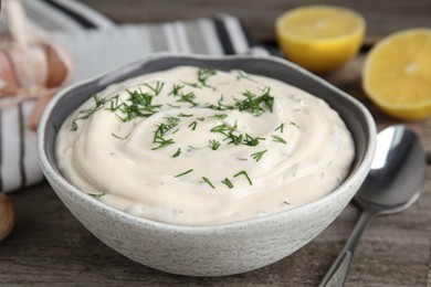 Tasty creamy dill sauce in bowl on wooden table, closeup