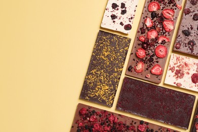 Photo of Different chocolate bars with freeze dried fruits on yellow background, flat lay. Space for text
