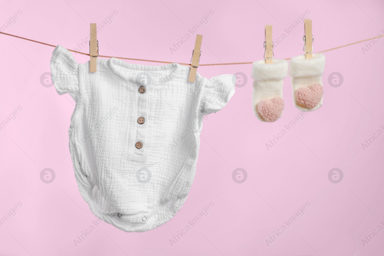Photo of Cute baby onesie and socks drying on washing line against pink background