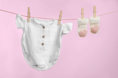 Photo of Cute baby onesie and socks drying on washing line against pink background