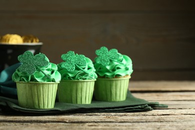 Photo of St. Patrick's day party. Tasty cupcakes with clover leaf toppers and green cream on wooden table, closeup. Space for text
