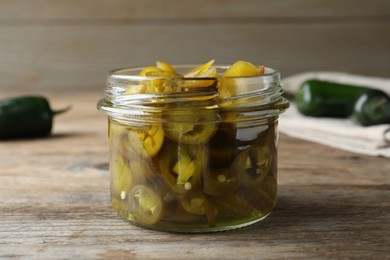 Glass jar with slices of pickled green jalapeno peppers on wooden table