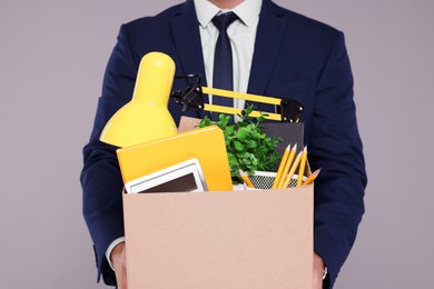 Photo of Unemployed man with box of personal office belongings on grey background, closeup