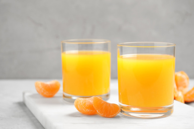 Photo of Glasses of fresh tangerine juice and fruits on light table