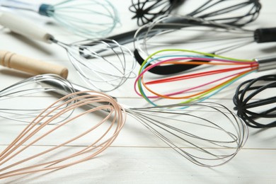 Different whisks on white wooden table, closeup