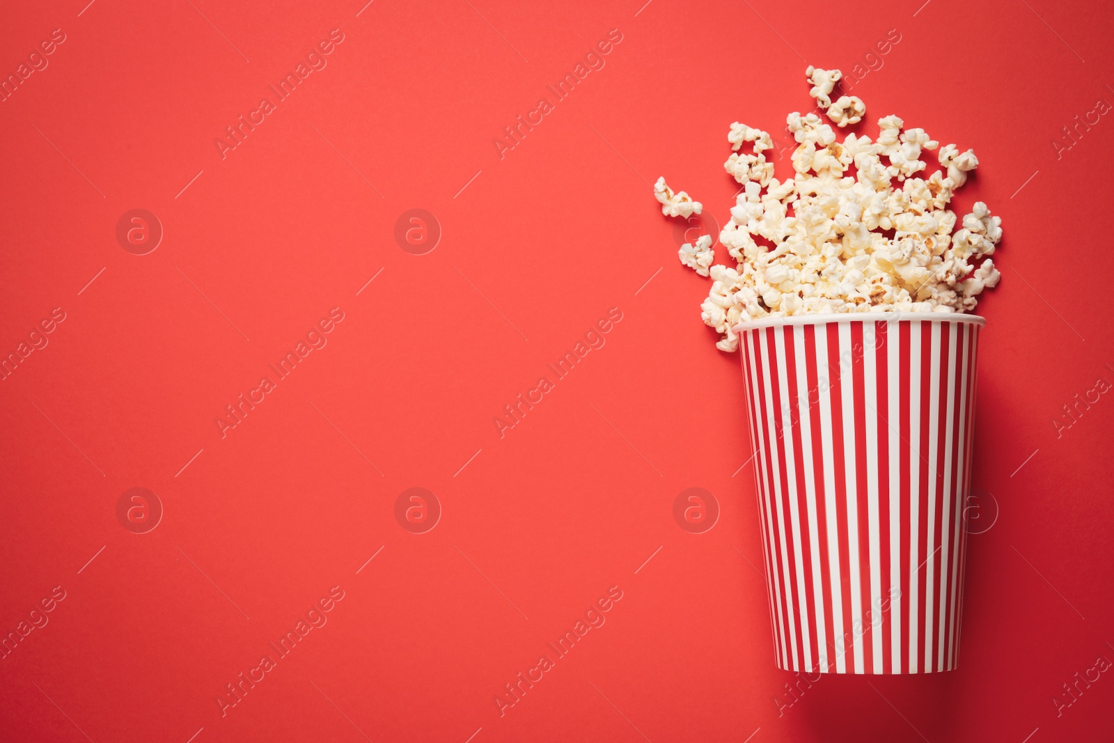 Photo of Overturned paper cup with delicious popcorn on red background, top view. Space for text