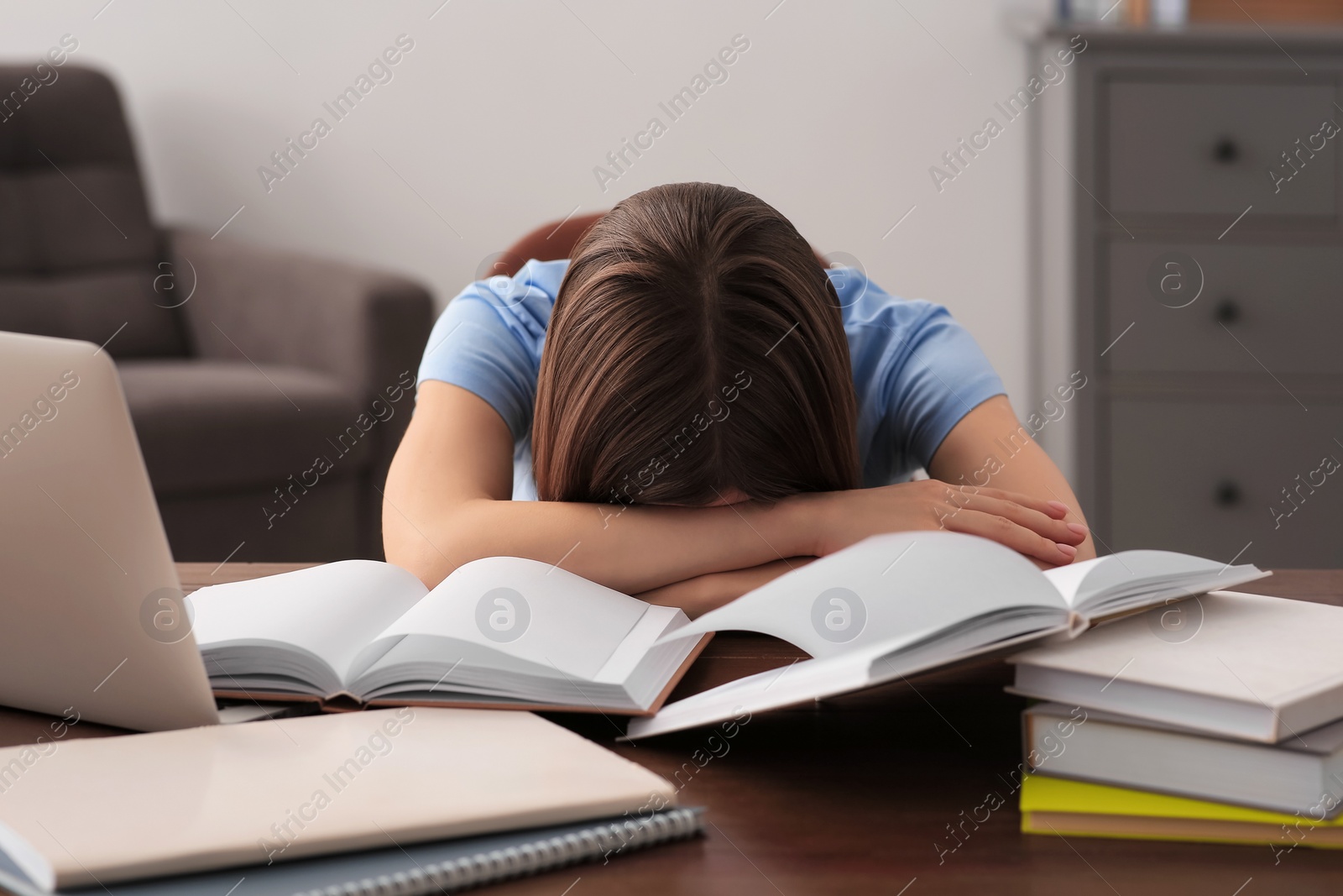 Photo of Young tired woman sleeping near books at wooden table indoors