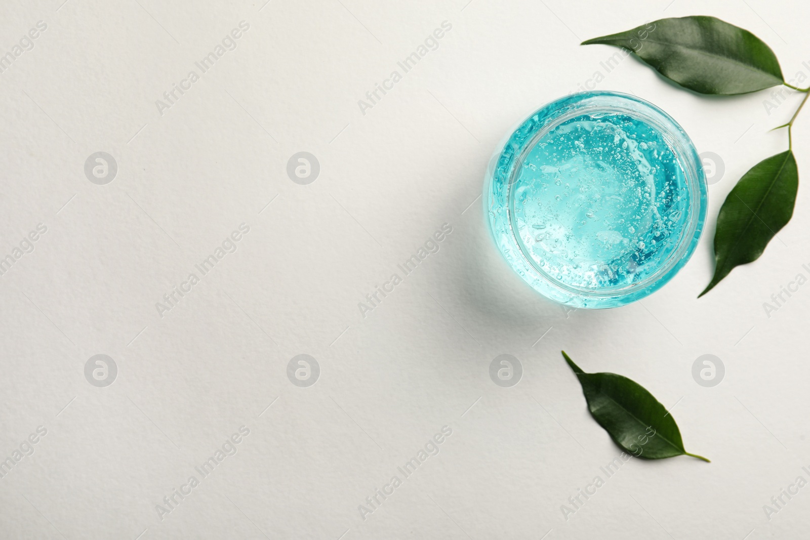 Photo of Jar of blue cosmetic gel and green leaves on white background, flat lay. Space for text