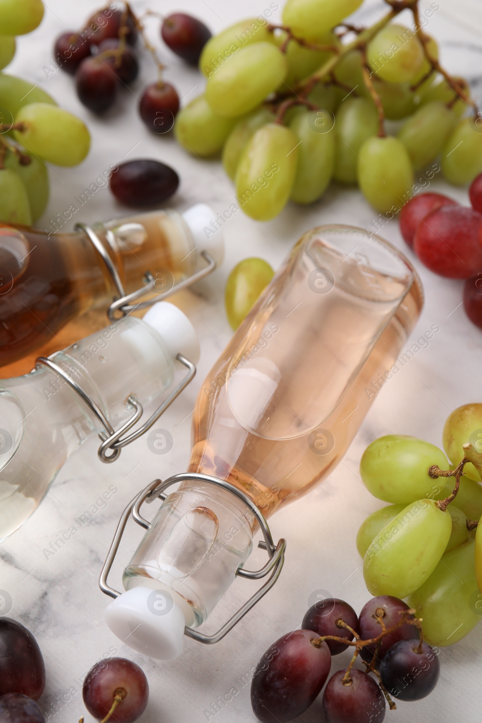 Photo of Different types of vinegar in bottles and grapes on light table, closeup