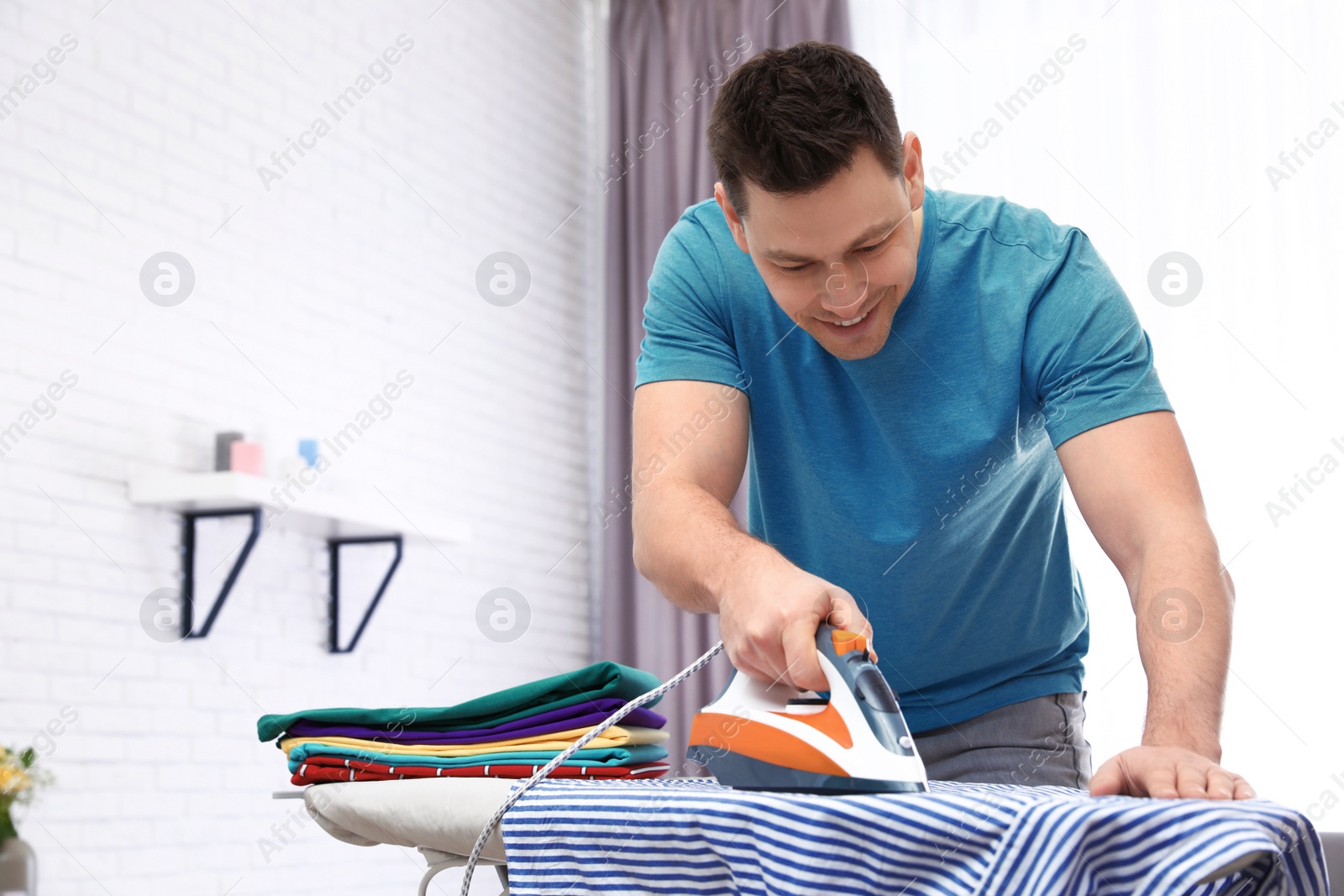 Photo of Man ironing shirt on board at home. Space for text