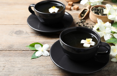 Photo of Cups of tea and fresh jasmine flowers on wooden table