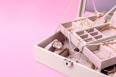 Jewelry box with many different accessories on pink background, closeup. Space for text