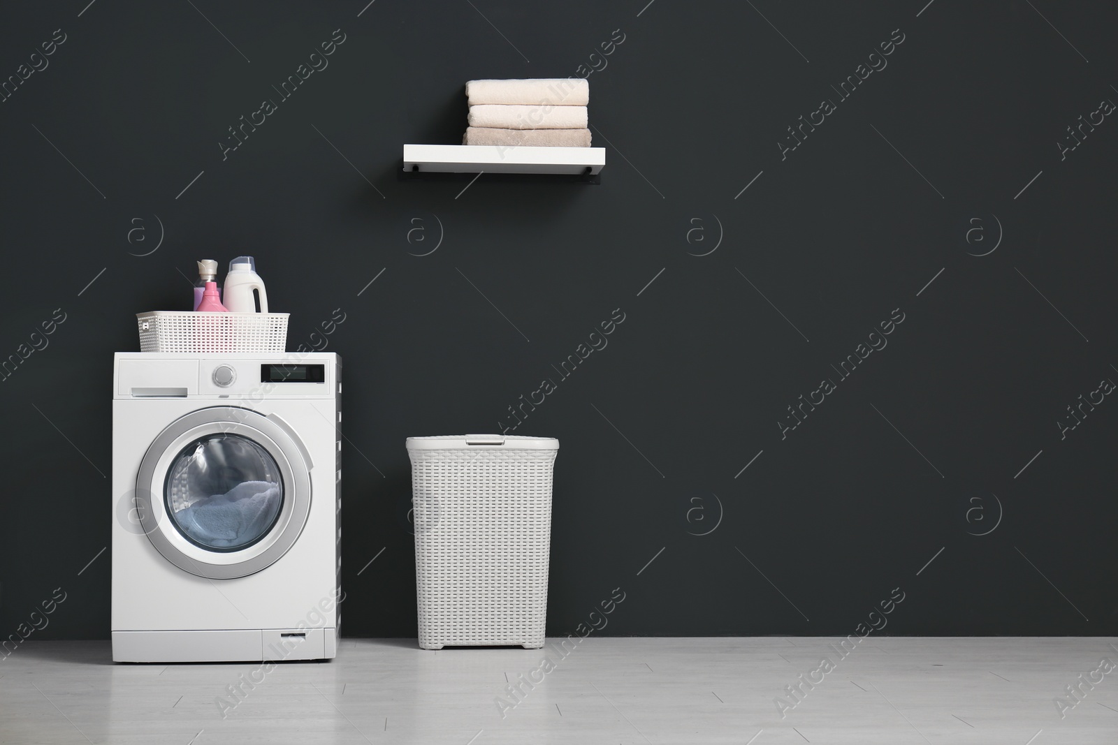 Photo of Modern washing machine, laundry basket and shelf with towels in bathroom. Space for text