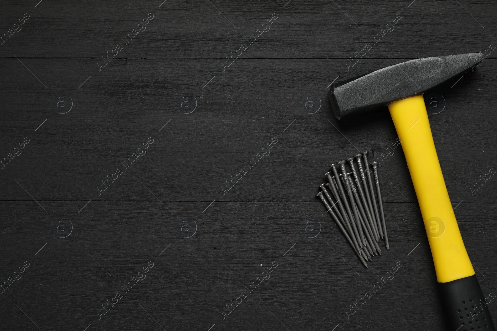 Photo of New hammer and metal nails on black wooden table, flat lay. Space for text