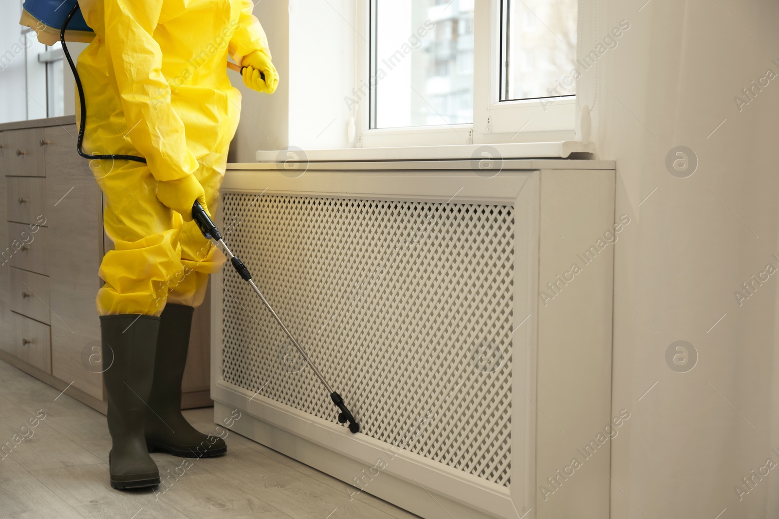 Photo of Pest control worker in protective suit spraying pesticide near window indoors, closeup