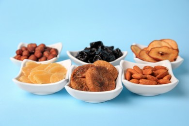 Bowls with dried fruits and nuts on light blue background
