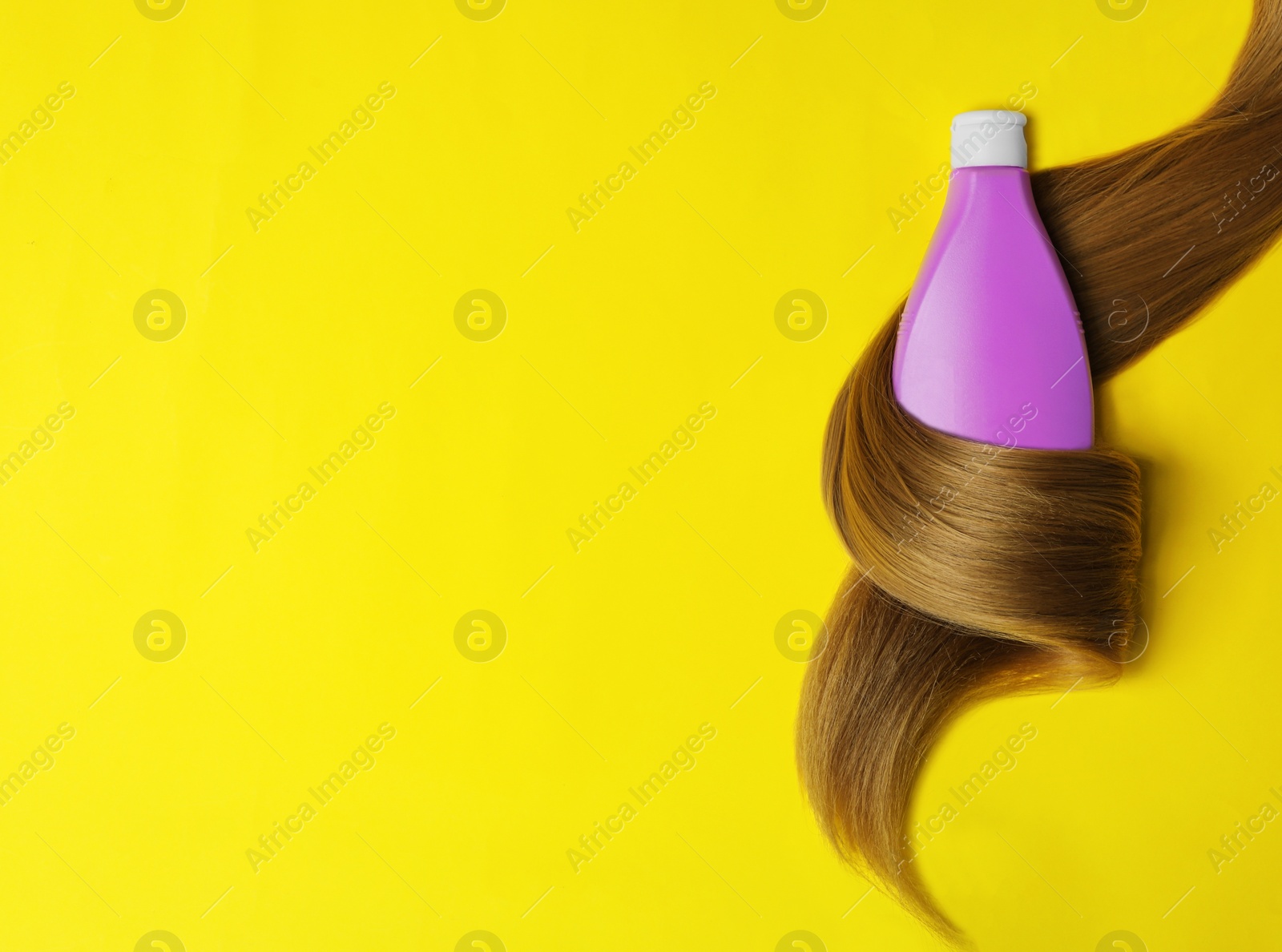 Photo of Shampoo bottle wrapped in lock of hair on yellow background, flat lay with space for text. Natural cosmetic products