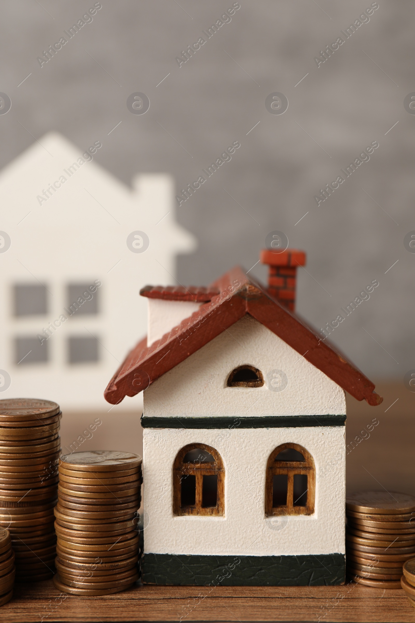 Photo of House models and stacked coins on wooden table against gray background