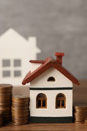 House models and stacked coins on wooden table against gray background