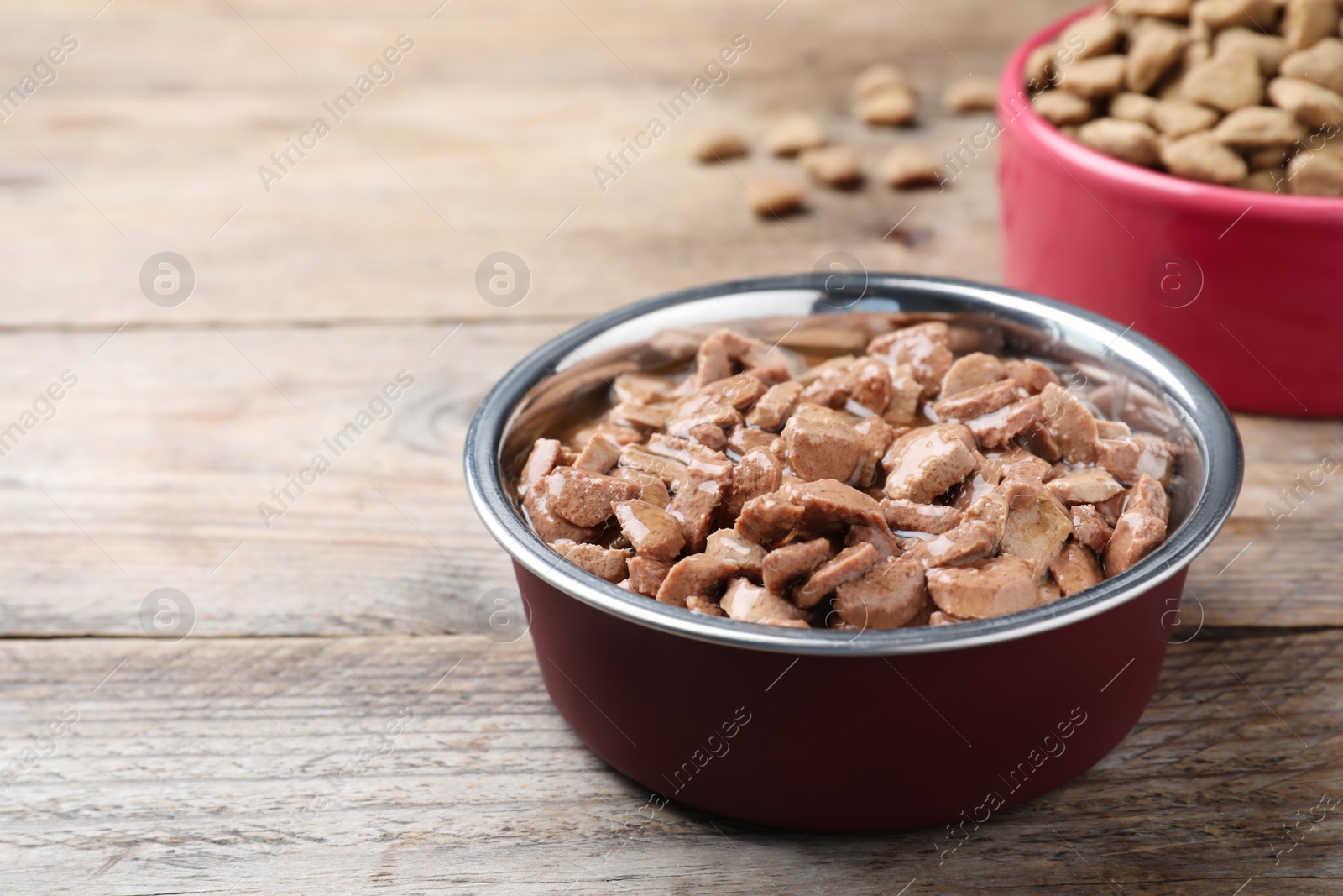 Photo of Wet pet food in feeding bowl on wooden table. Space for text