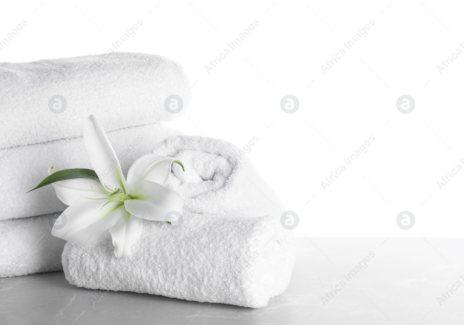 Photo of Fresh towels and lily flower on light grey marble table against white background. Space for text