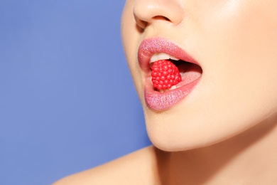 Photo of Beautiful young model with creative makeup holding candy in lips on color background