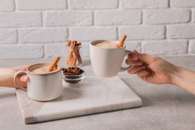 Women holding glass cups of delicious eggnog with cinnamon and anise at light grey table, closeup