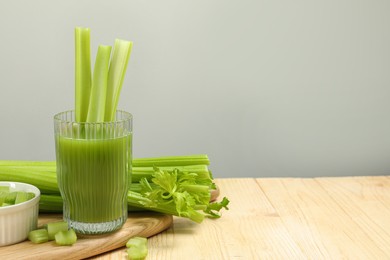 Photo of Glass of celery juice and fresh vegetables on wooden table, space for text