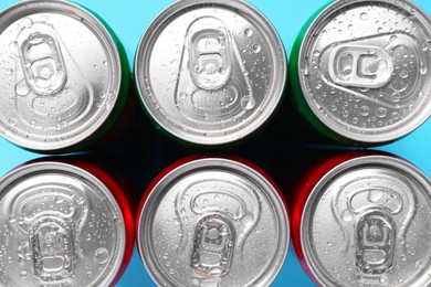 Photo of Energy drinks in wet cans on light blue background, top view