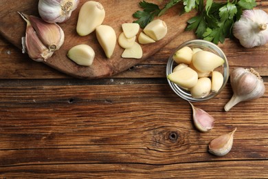 Photo of Flat lay composition with fresh garlic bulbs and cloves on wooden table, space for text. Organic product