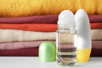 Different deodorants near stack of clean clothes on white table