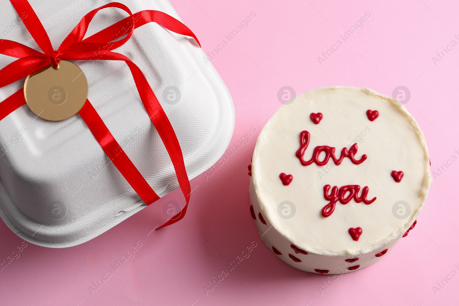 Photo of Bento cake with text Love You and takeaway packaging on pink table, above view. St. Valentine's day surprise