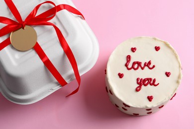 Photo of Bento cake with text Love You and takeaway packaging on pink table, above view. St. Valentine's day surprise