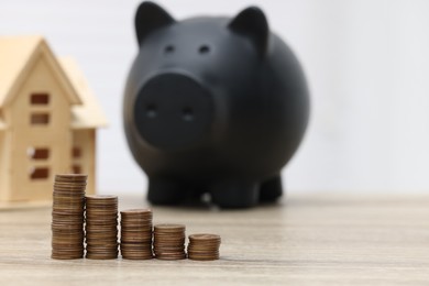 Photo of House model, piggy bank and stacked coins on wooden table, selective focus