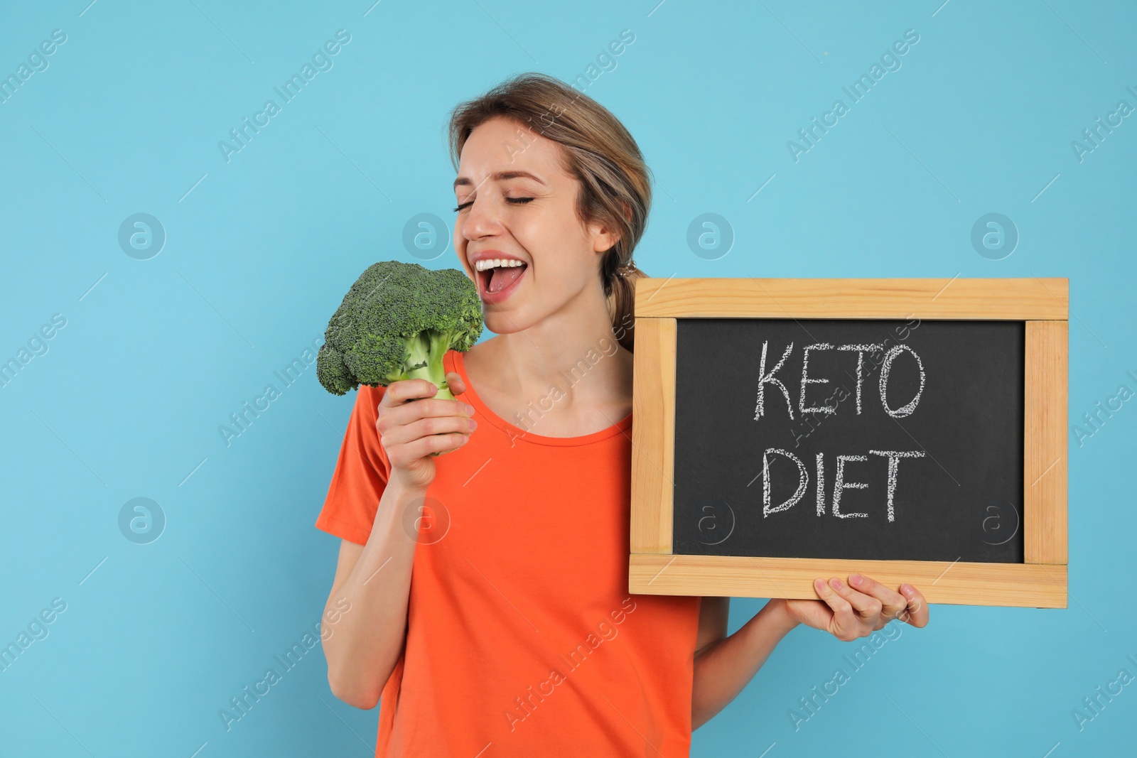 Photo of Woman holding blackboard with phrase Keto Diet and broccoli on light blue background