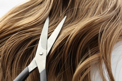 Photo of Scissors and brown wavy hair on white background, closeup. Hairdresser service