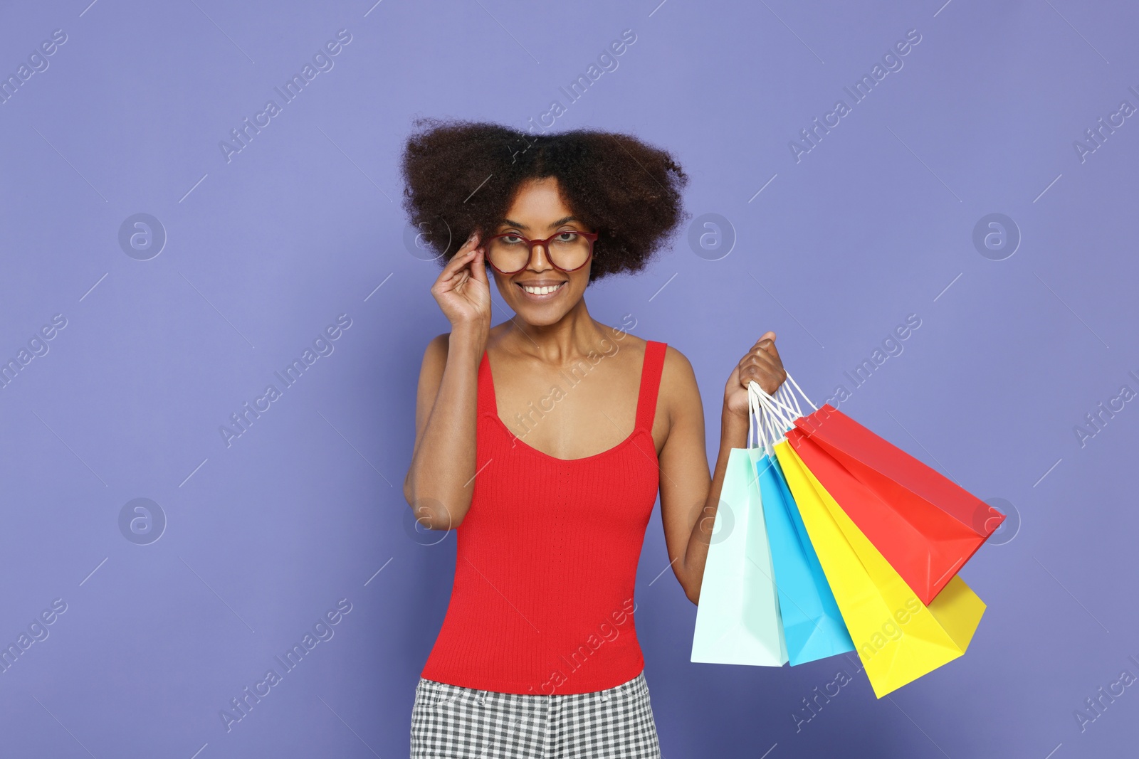 Photo of Happy African American woman in glasses with shopping bags on purple background