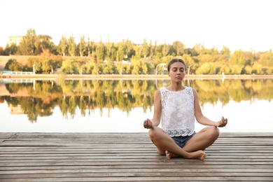 Photo of Young woman meditating near river at sunset, space for text. Nature healing power