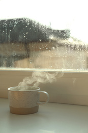 Photo of Cup of hot drink near window on rainy day. Space for text