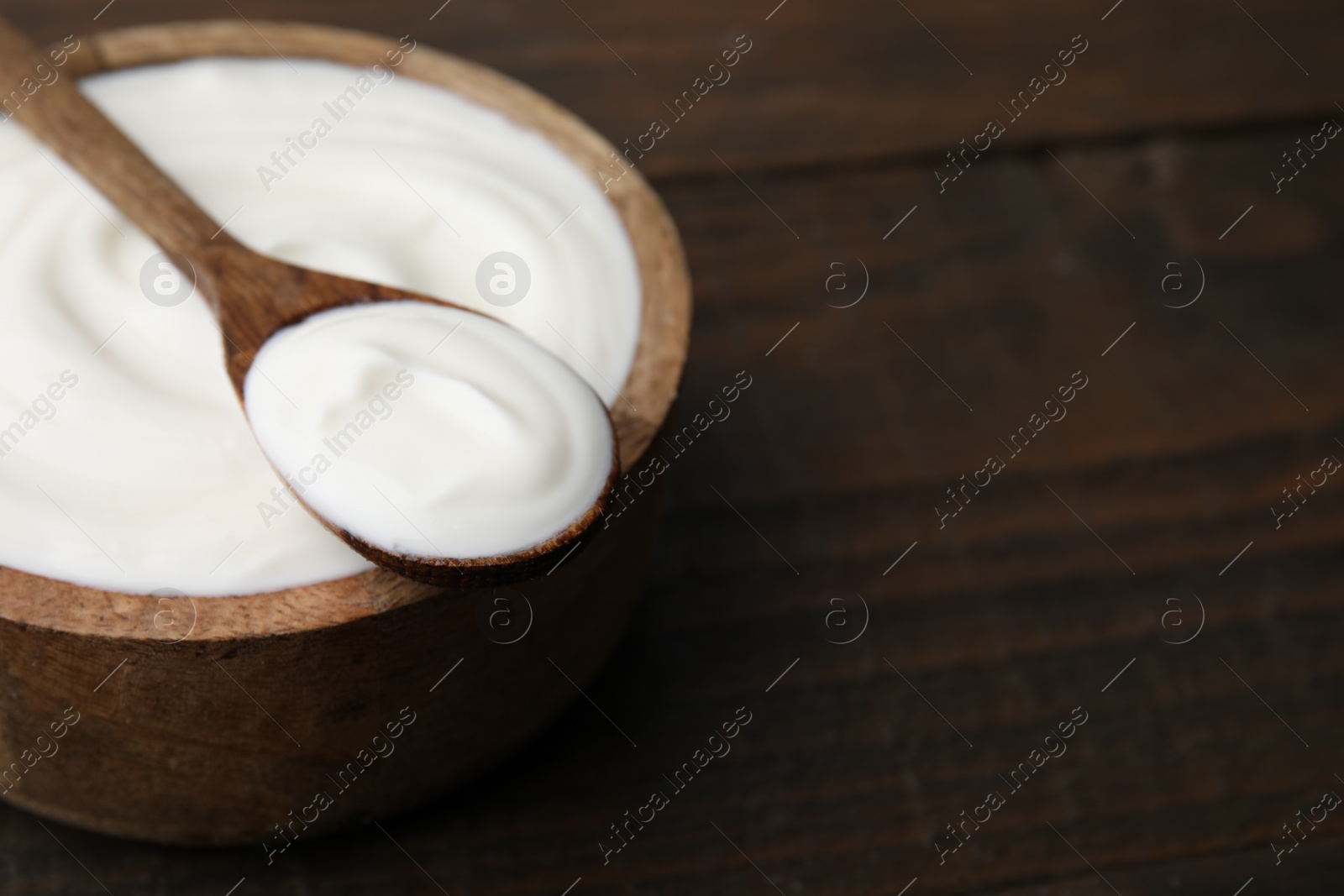 Photo of Delicious natural yogurt in bowl and spoon on wooden table, closeup. Space for text