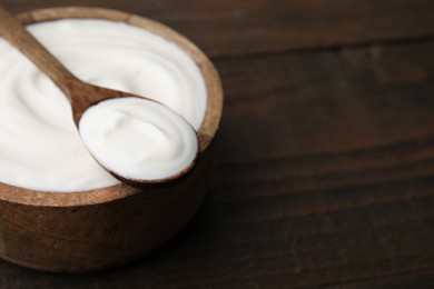 Photo of Delicious natural yogurt in bowl and spoon on wooden table, closeup. Space for text